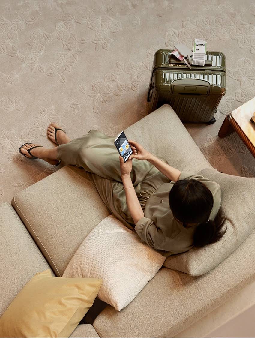 Image of a woman sitting on her couch adjusting her thermostat with Google home product from her mobile device