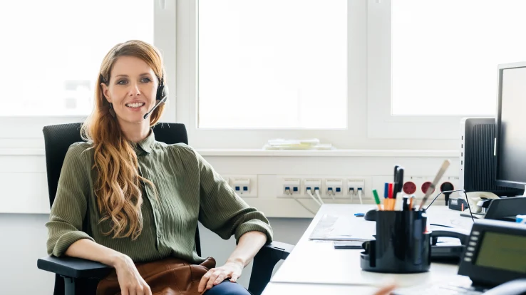 Woman with headset at desk in office.