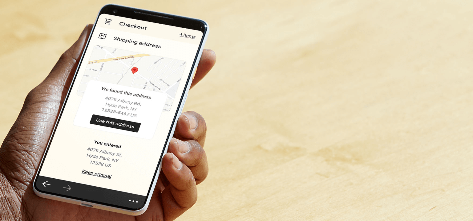 Main tenant un smartphone affichant un écran de vérification d'adresse de livraison avec une épingle sur la carte lors d'un paiement mobile.