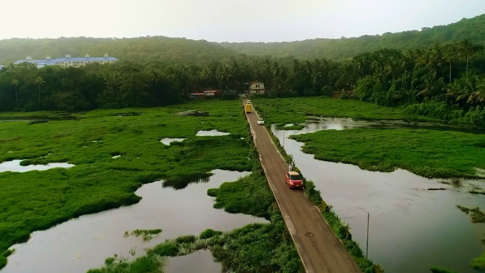 Los coches cruzan un estrecho puente sobre un exuberante pantano verde rodeado de densas colinas tropicales y cielos brumosos.