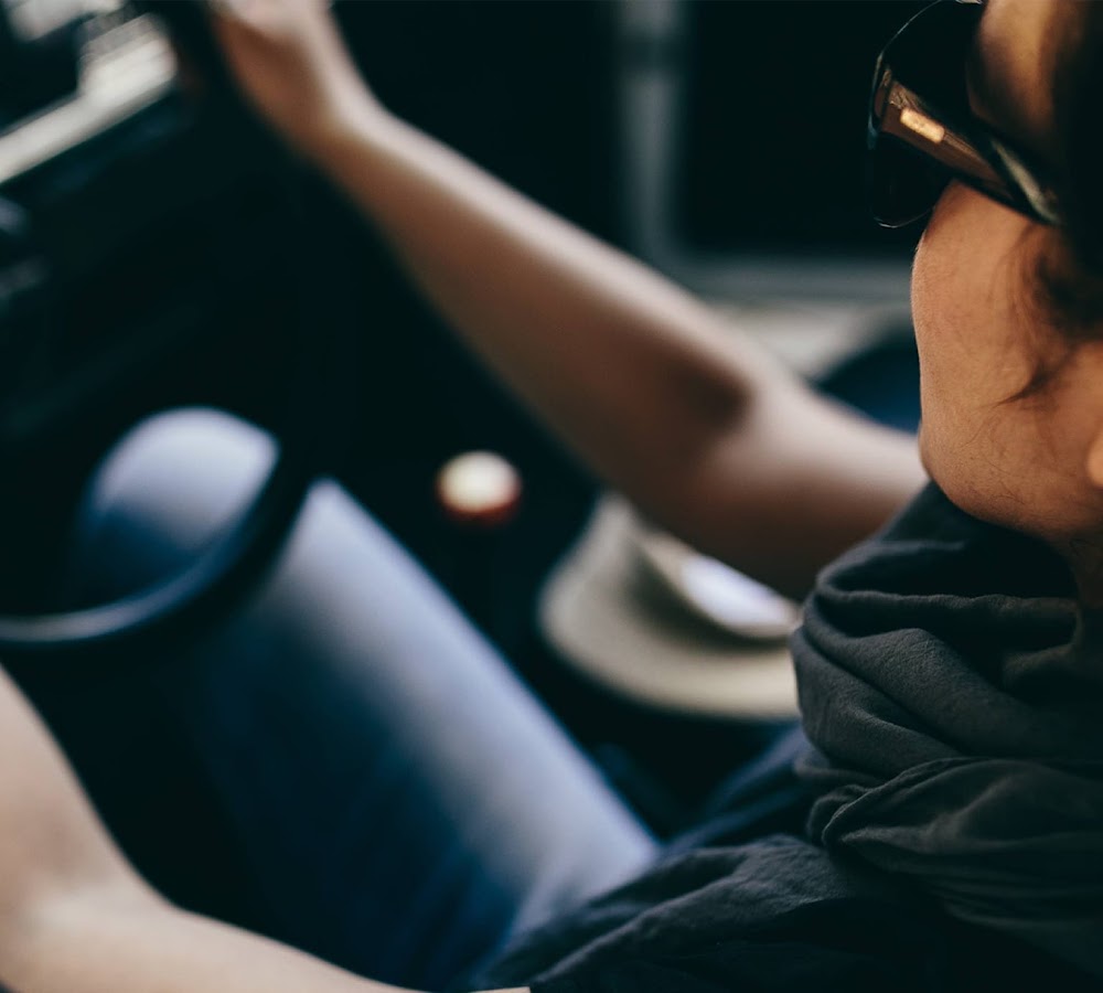 A woman with sun glasses on wheel driving using Hey Google to play music