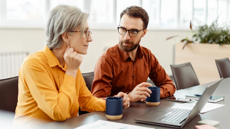 Man and woman in a conference room working together on a laptop. 